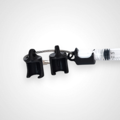 Three black polylactic acid created using additive manufacturing classic cap clips on steel cable keyring. Featured attached to a syringe. Shown on a white background.