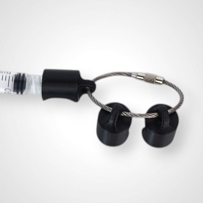 Three black polylactic acid created using additive manufacturing classic cap clips on steel cable keyring. Featured attached to a syringe. Shown on a white background.
