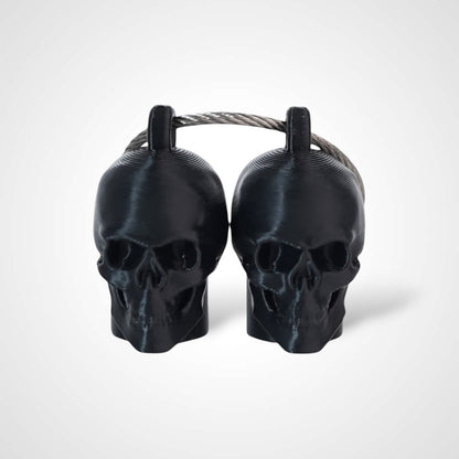 Two black polylactic acid created using additive manufacturing skull cap clips on steel cable keyring. Shown on a white background.