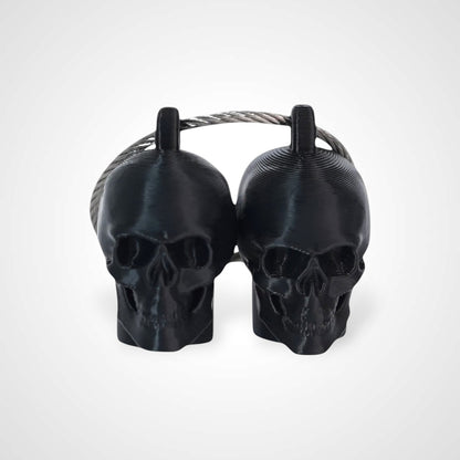 Two black polylactic acid created using additive manufacturing skull cap clips on steel cable keyring. Shown on a white background.