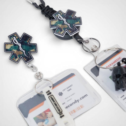 Camo Star badge reel. On a carabiner with a steel retractable cable next to a swivel-alligator clip that rotates 360° with a nylon retractable string. Shown on a white background. 