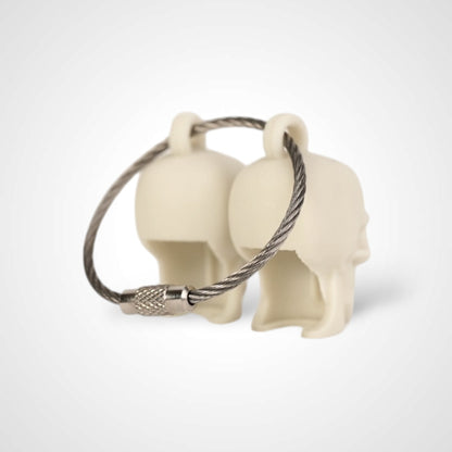 Two off white polylactic acid created using additive manufacturing skull cap clips on steel cable keyring. Shown on a white background.