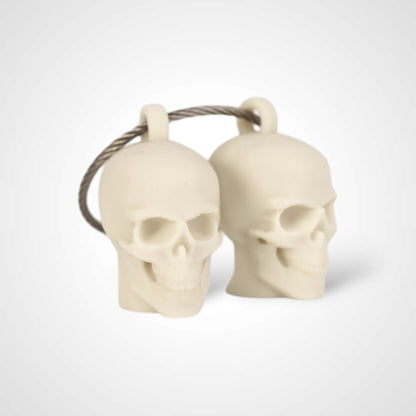 Two off white polylactic acid created using additive manufacturing skull cap clips on steel cable keyring. Shown on a white background.