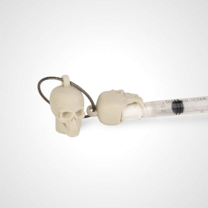 Two off white polylactic acid created using additive manufacturing skull cap clips on steel cable keyring. Featured attached to a syringe. Shown on a white background.