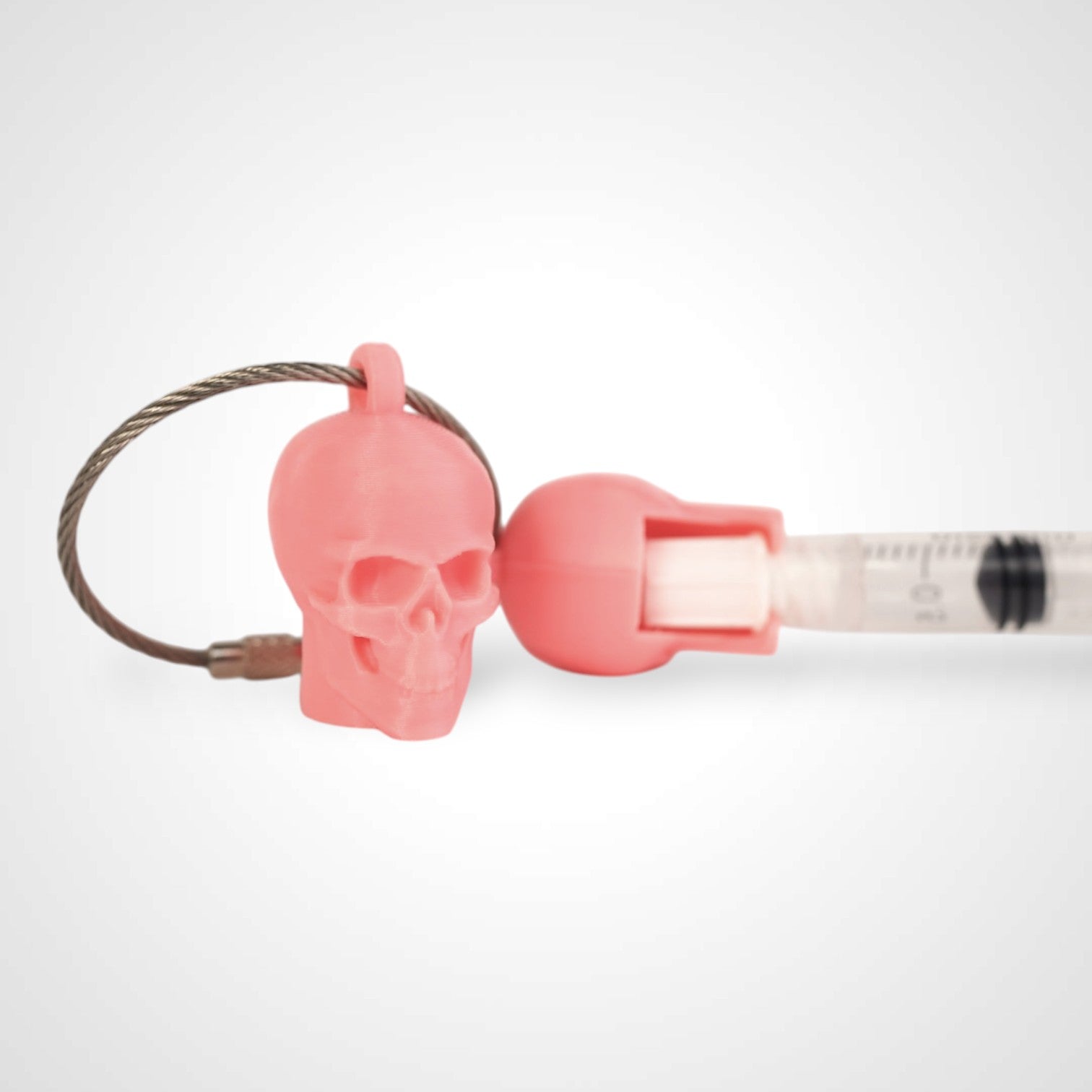 Two pink polylactic acid created using additive manufacturing skull cap clips on steel cable keyring. Featured attached to a syringe. Shown on a white background.