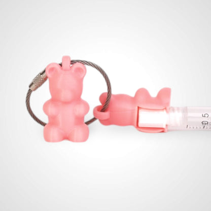 Two pink polylactic acid created using additive manufacturing gummy bear cap clips on steel cable keyring. Featured attached to a syringe. Shown on a white background.