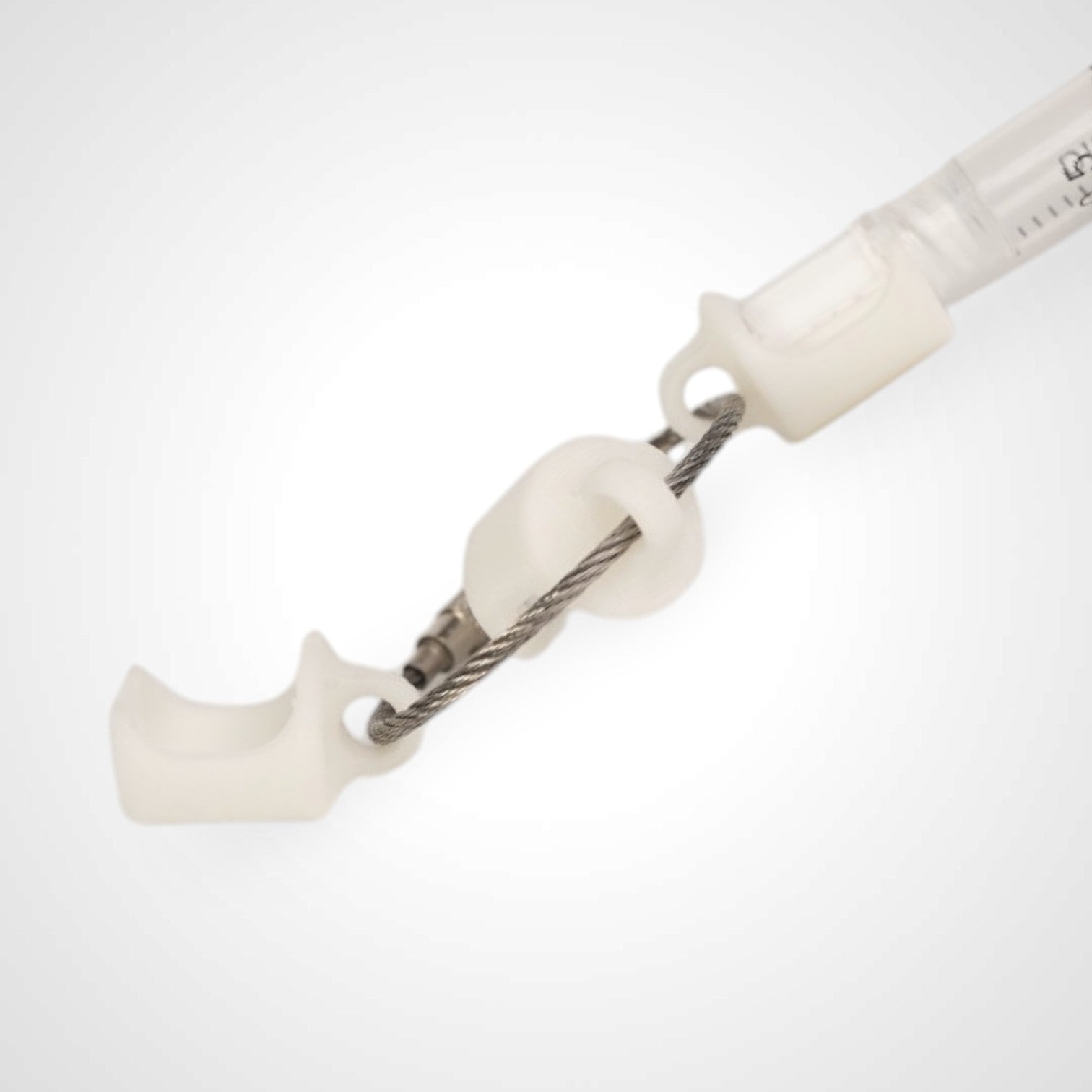 Three white polylactic acid created using additive manufacturing classic cap clips on steel cable keyring. Featured attached to a syringe. Shown on a white background.