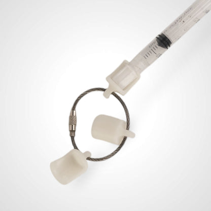 Three white polylactic acid created using additive manufacturing classic cap clips on steel cable keyring. Featured attached to a syringe. Shown on a white background.