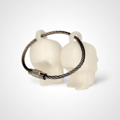 Two white polylactic acid created using additive manufacturing skull cap clips on steel cable keyring. Shown on a white background.