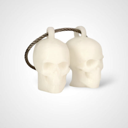 Two white polylactic acid created using additive manufacturing skull cap clips on steel cable keyring. Shown on a white background.
