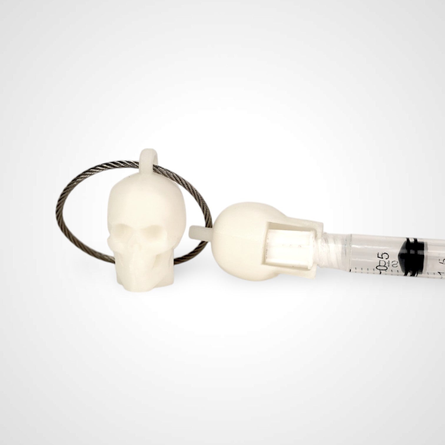 Two white polylactic acid created using additive manufacturing skull cap clips on steel cable keyring. Featured attached to a syringe. Shown on a white background.