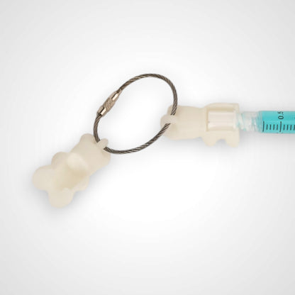 Two white polylactic acid created using additive manufacturing gummy bear cap clips on steel cable keyring. Featured attached to a syringe. Shown on a white background.