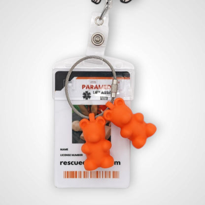 Two orange polylactic acid created using additive manufacturing gummy bear cap clips on steel cable keyring. Featured attached to a badge. Shown on a white background.