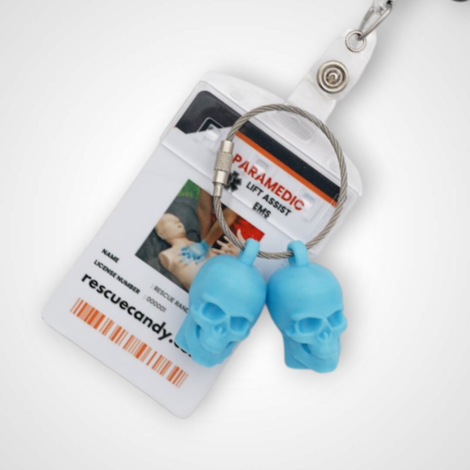 Two blue polylactic acid created using additive manufacturing skull cap clips on steel cable keyring. Featured attached to a badge. Shown on a white background.