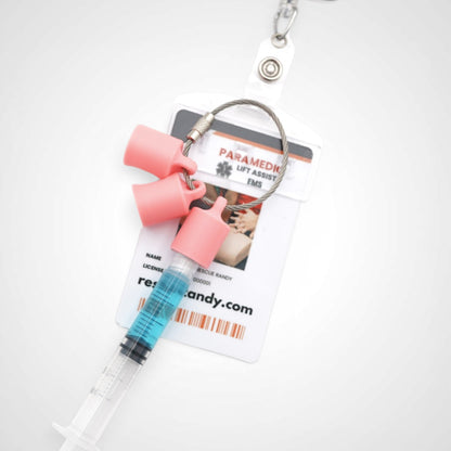 Three pink polylactic acid created using additive manufacturing classic cap clips on steel cable keyring. Featured attached to a syringe and on a badge. Shown on a white background.
