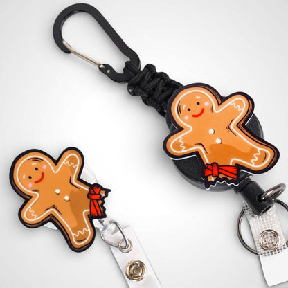 Tourniquet gingerbread man badge reel. On a carabiner with a steel retractable cable next to a swivel-alligator clip that rotates 360° with a nylon retractable string. Shown on a white background. 