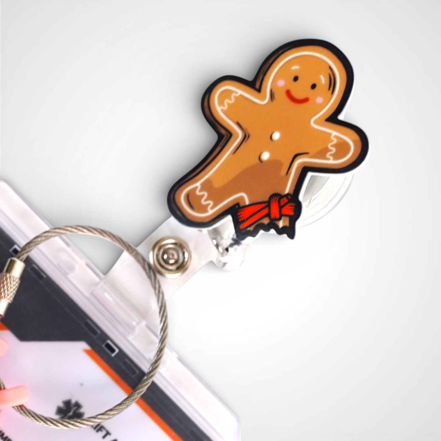 Tourniquet gingerbread man badge reel. On a swivel-alligator clip that rotates 360° with a nylon retractable string. Shown on a white background.