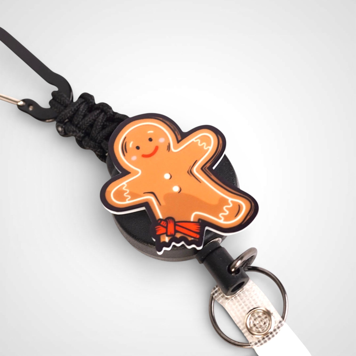 Tourniquet gingerbread man badge reel. On a carabiner with a steel retractable cable. Shown on a white background.