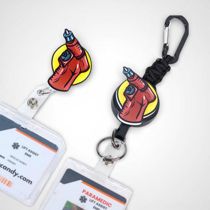 IO Drill badge reel. On a swivel-alligator clip that rotates 360° with a nylon retractable string next to a carabiner with a steel retractable cable.Shown on a white background.
