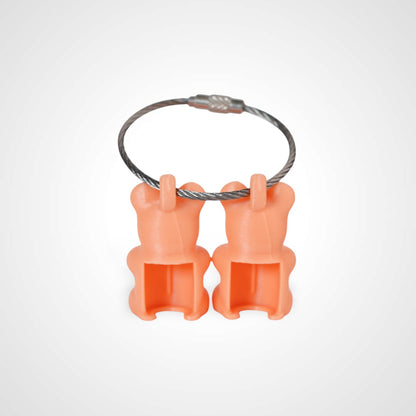 Two orange polylactic acid created using additive manufacturing gummy bear clips on steel cable keyring. Shown on a white background.