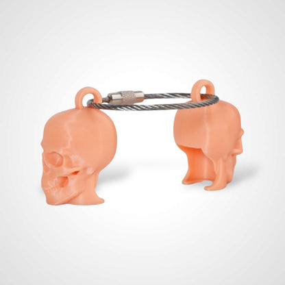 Two orange polylactic acid created using additive manufacturing skull cap clips on steel cable keyring. Shown on a white background.