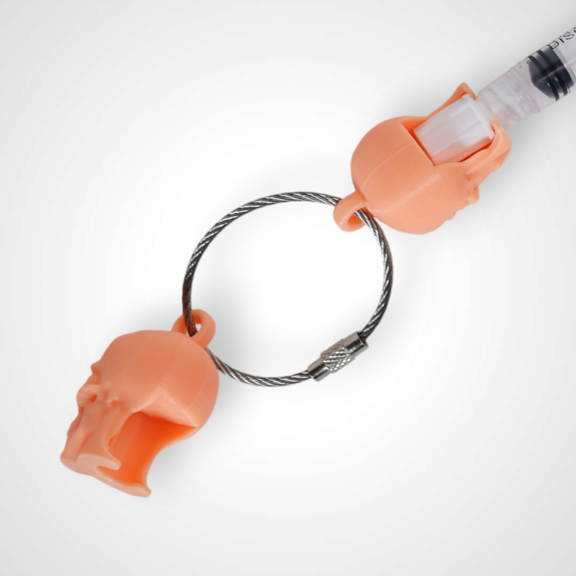 Two orange polylactic acid created using additive manufacturing skull cap clips on steel cable keyring. Featured attached to a syringe. Shown on a white background.