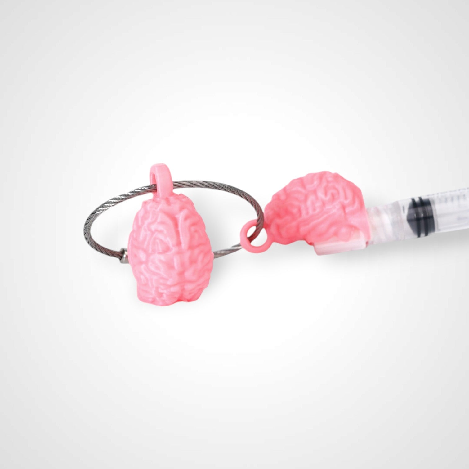 Two pink polylactic acid created using additive manufacturing anatomical brain cap clips on steel cable keyring. Featured attached to a syringe. Shown on a white background.