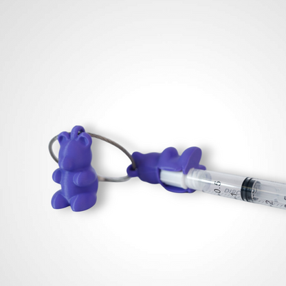 Two purple polylactic acid created using additive manufacturing gummy bear clips on steel cable keyring. Featured attached to a syringe. Shown on a white background.