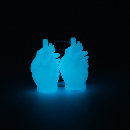 Two blue polylactic acid created using additive manufacturing anatomical heart cap clip on steel cable keyring. Shown glowing blue with black background.