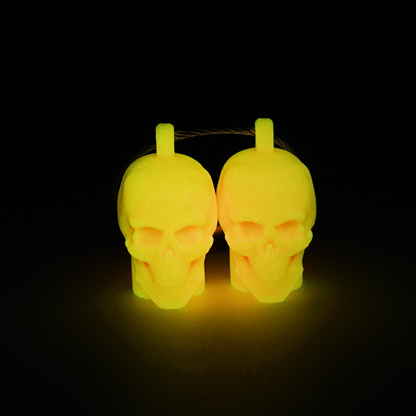 Two orange polylactic acid created using additive manufacturing skull cap clips on steel cable keyring. Shown glowing yellow on a black background.