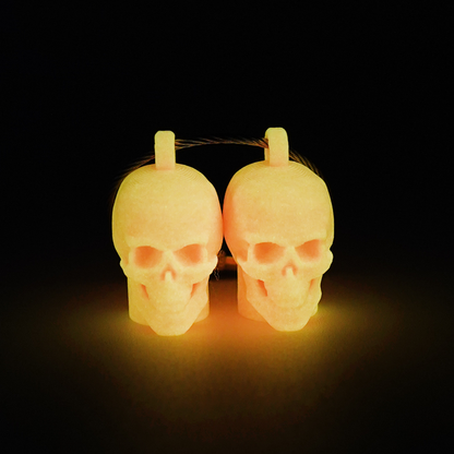 Two pink polylactic acid created using additive manufacturing skull cap clips on steel cable keyring. Shown glowing orange on a black background.