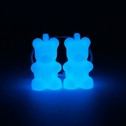 Two white polylactic acid created using additive manufacturing gummy bear cap clips on steel cable keyring. Shown glowing blue on black background.